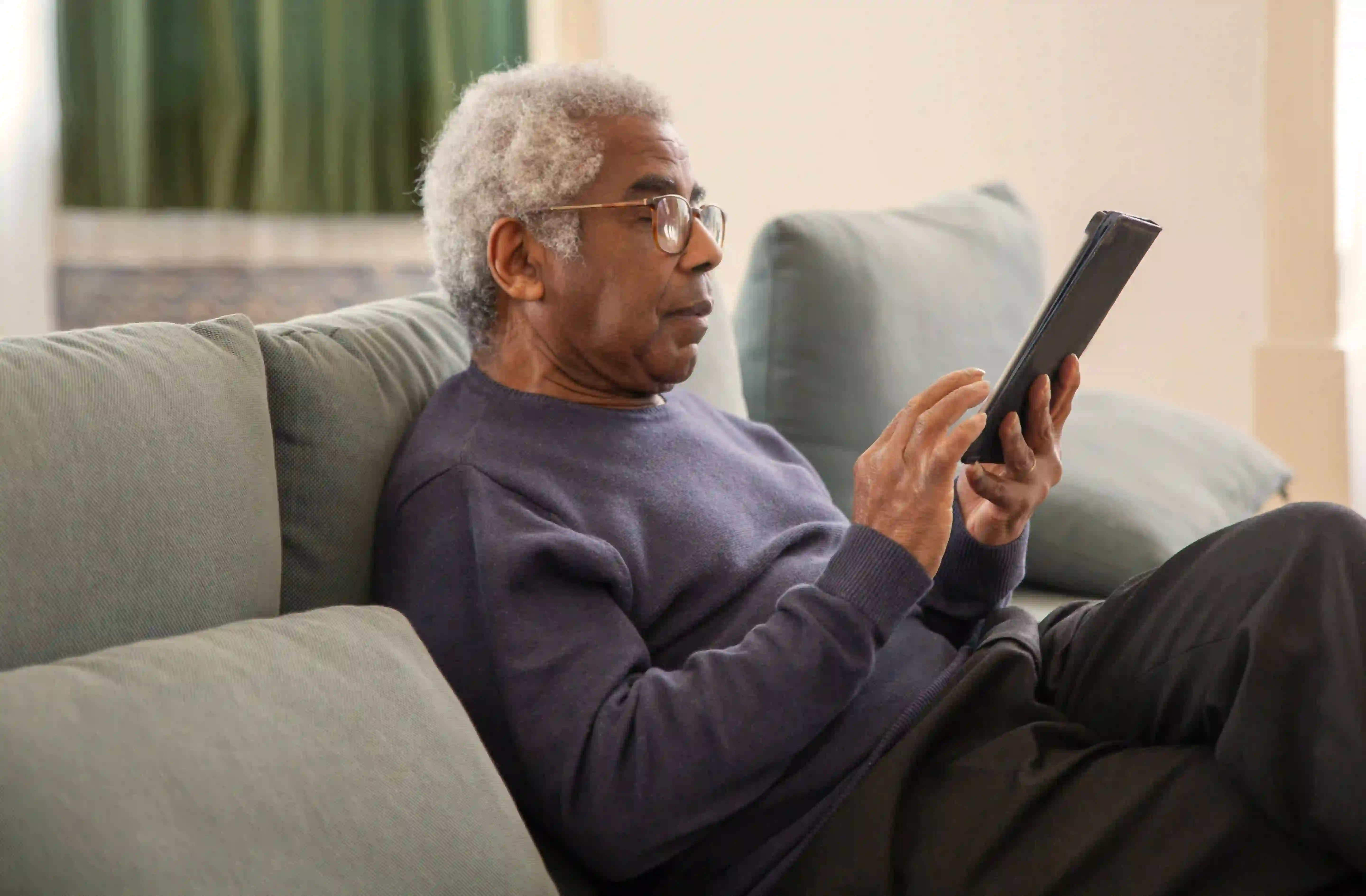 Man sitting on his couch and browsing his tablet.